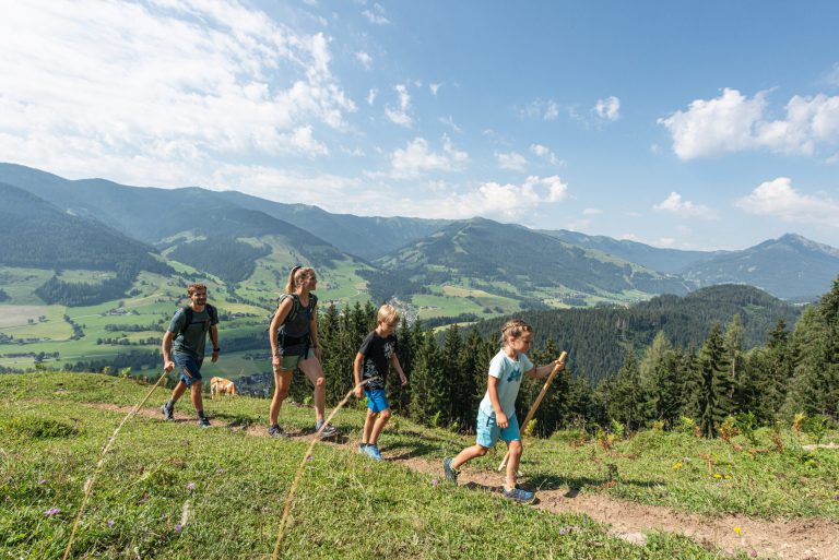 Familie wandert in den Alpen, umgeben von grünen Wiesen und Bergen, bei Thomanhof in Saalfelden.