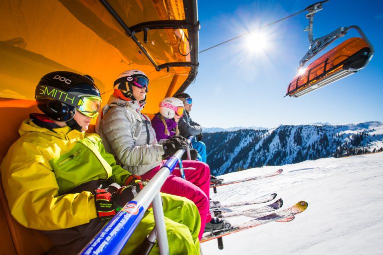 Familien genießen beim Skifahren in den Alpen sonnige Tage auf einem Skilift.